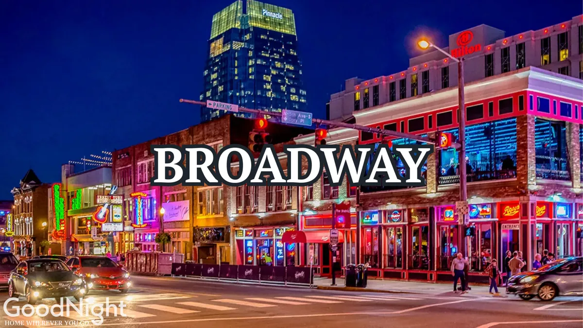 A bustling urban street at night illuminated by bright neon signs, with crowds of people walking along busy sidewalks. Tall buildings and energetic activity hint at Nashville’s famous nightlife and live music scene.