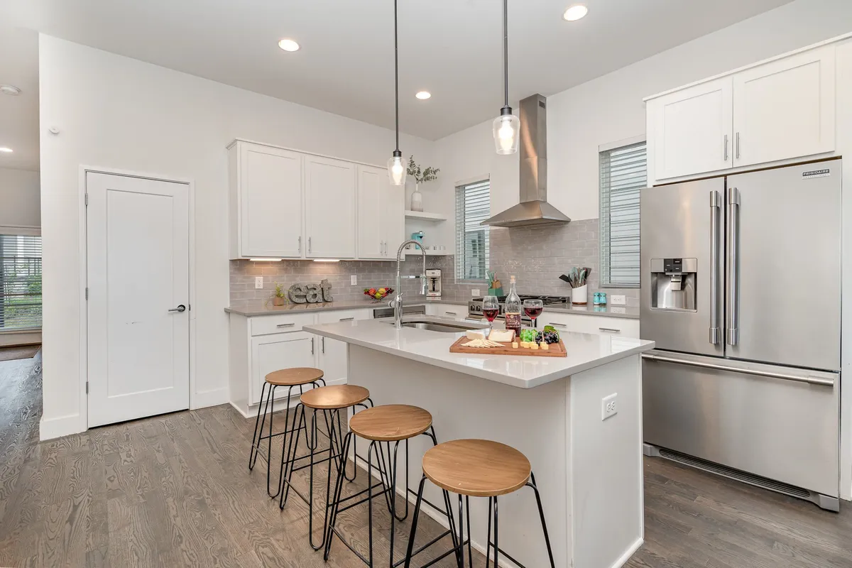 A stylish kitchen with a central island, bar stools, wine glasses set out for guests, and appealing decorative touches. This space invites casual breakfasts, group cooking sessions, or evening cocktails, with a focus on sociability and contemporary comfort.