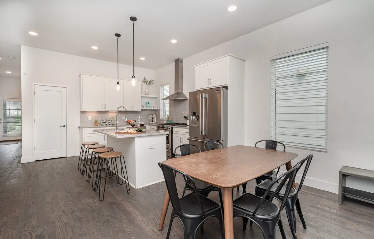 A modern kitchen and dining area featuring a kitchen island, modern appliances, and a large dining table. The space looks warm and welcoming, ideal for preparing meals, socializing, and hosting group activities.