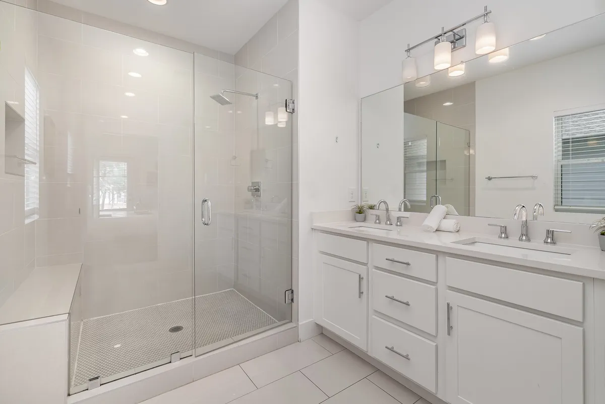 A modern bathroom featuring a glass shower enclosure, dual sink vanity, and stylish light fixtures. The space exudes a serene and refreshing mood, perfect for both morning routines and evening relaxation.
