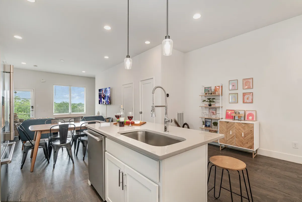 A modern interior with a kitchen island, adjacent dining table, and open shelving. The space flows seamlessly from the kitchen to the dining area, with a television visible from both spaces, emphasizing togetherness and convenience for group gatherings.